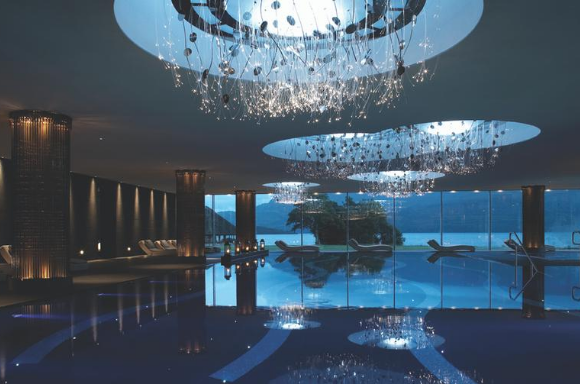 Calm indoor pool with light fixtures above and lounging seats behind