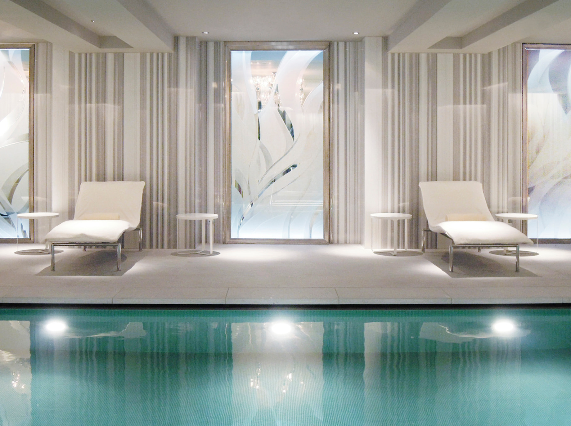 Calm indoor pool with reclined seats and white decoration