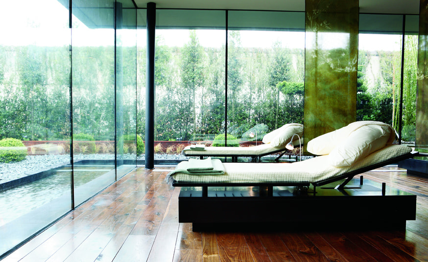 Two reclined beds look out through a glass wall onto greenery.