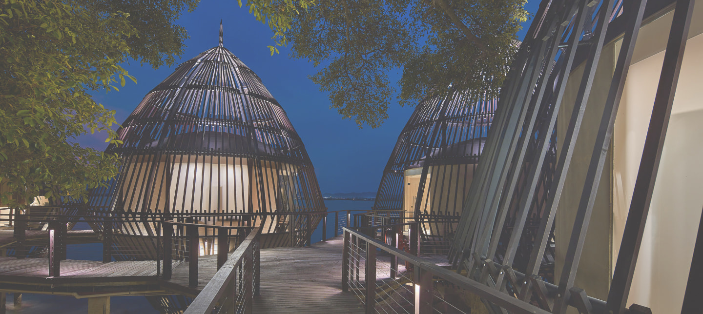 Pod-like rooms connected with wooden walkways, suspended by stilts over a shoreline.